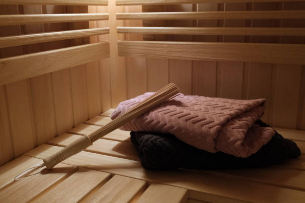 A bamboo sauna massage whisk is placed on two pink and gray towels on a wooden sauna shelf
