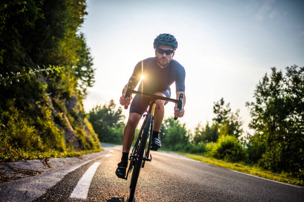 Front view of fit mid 20s Caucasian male approaching camera while standing and pedaling up mountain road during morning workout.