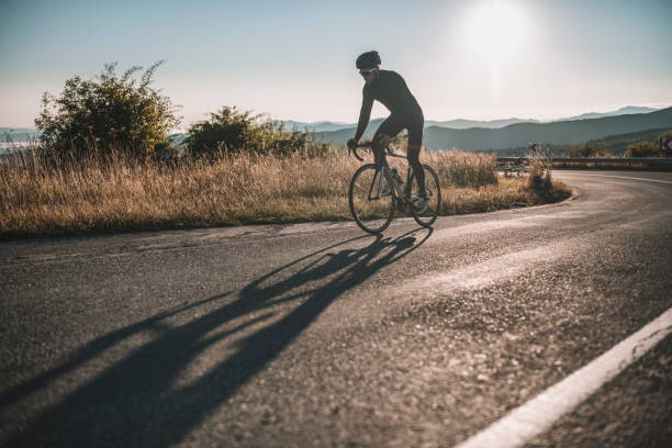 Male road cyclist is driving up on the road at sunrise.